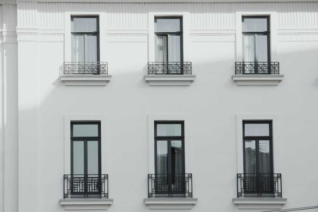 A minimalist view of a white building facade featuring black metal railings and symmetrically aligned windows.